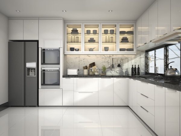 White gloss L-shaped kitchen with lit glass-front upper cabinets and built-in ovens